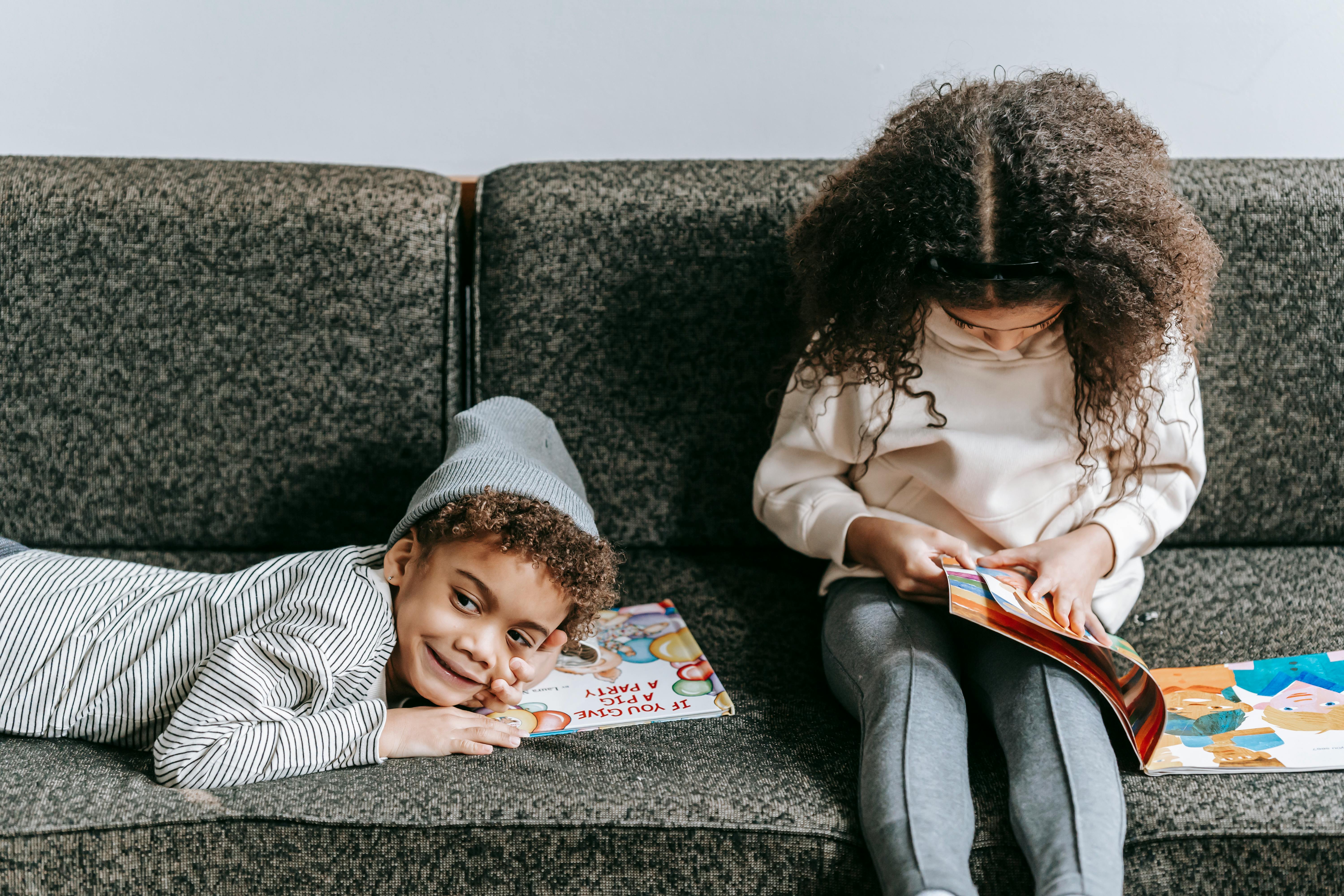 happy black siblings resting on sofa with books