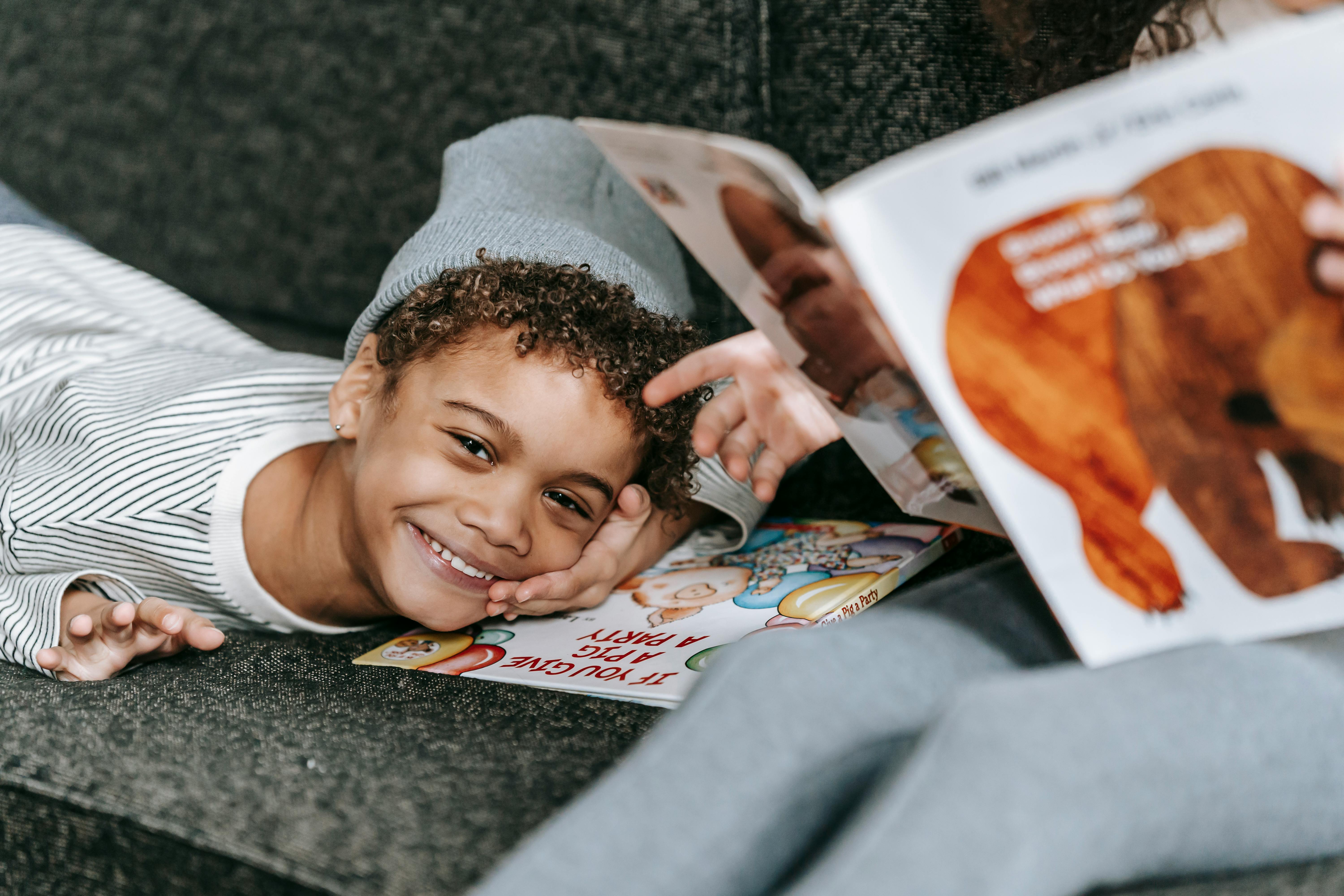 joyful black boy lying on couch with books