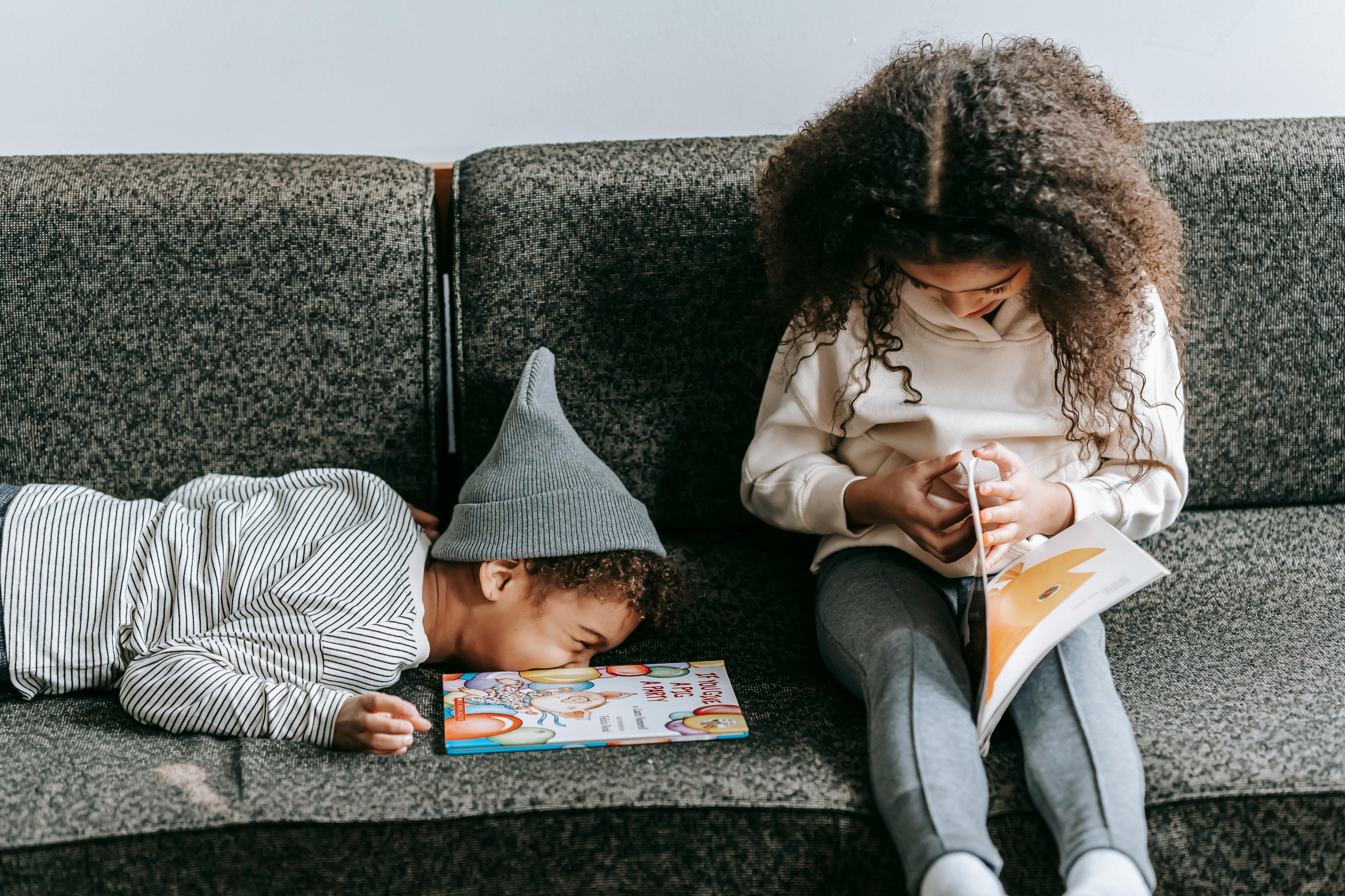 laughing black boy lying on sofa near reading sister