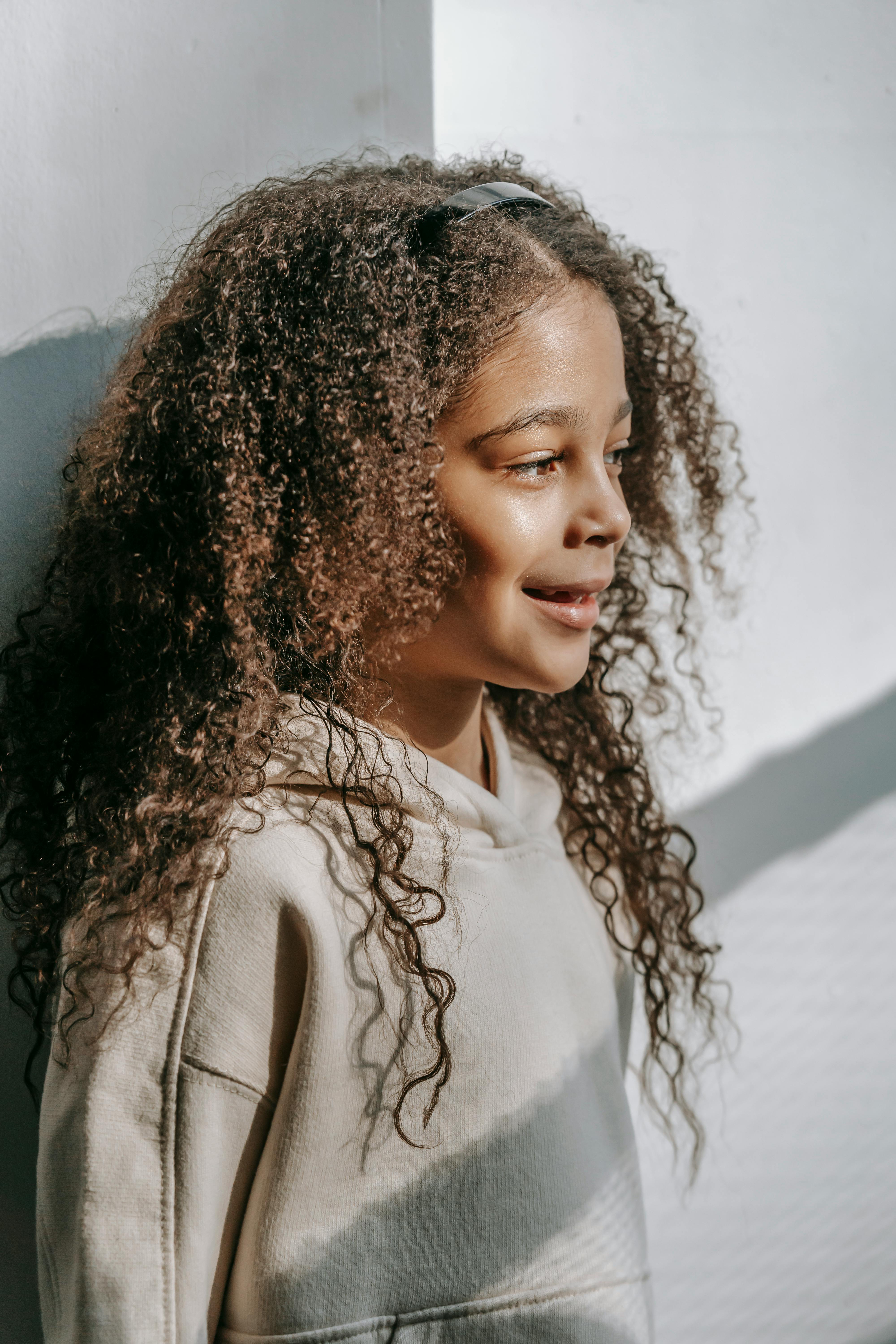 Cheerful black girl with long curly hair looking away against white wall ·  Free Stock Photo