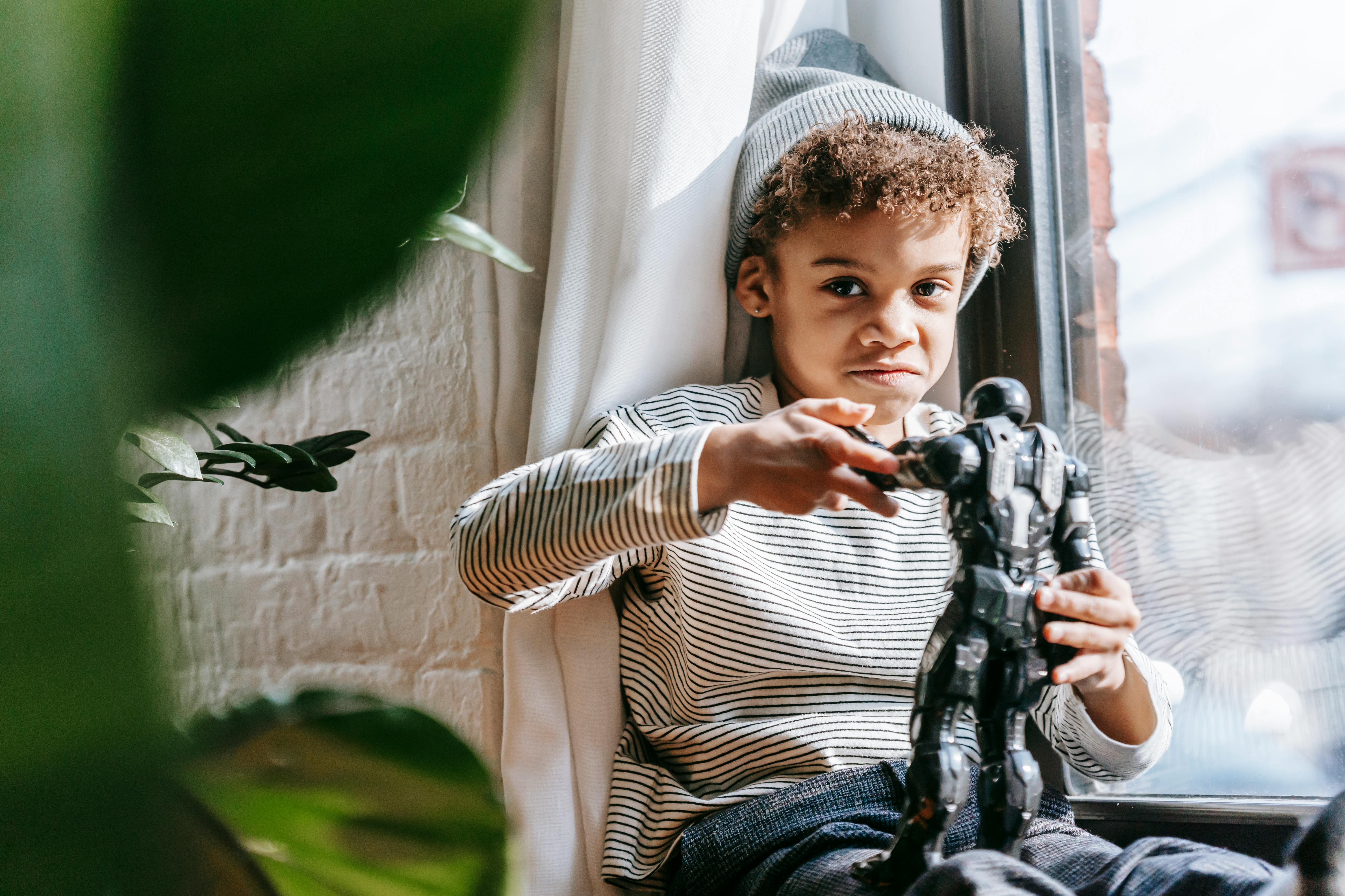 cheerful black boy playing with toy at home in sunny day