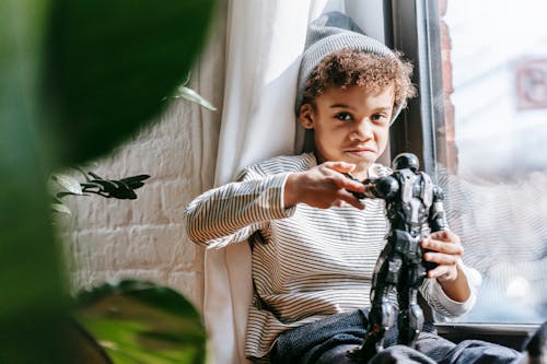 Cheerful black boy playing with toy at home in sunny day