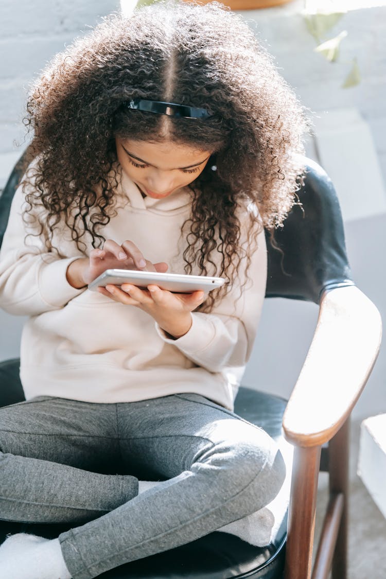 Pensive Black Girl Browsing Tablet In Light Room In Sunny Day