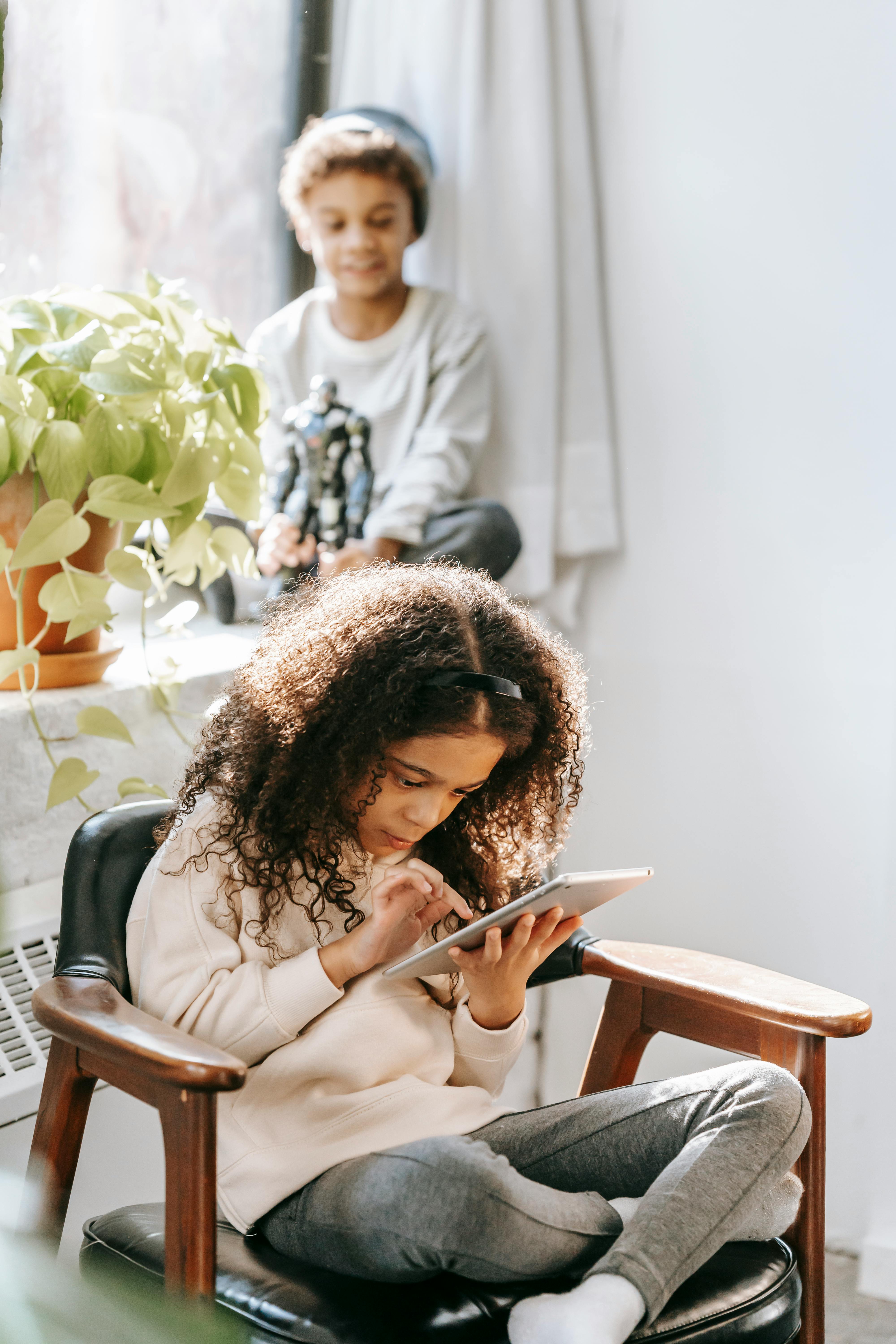 concentrated black girl using tablet while spending time with brother at home