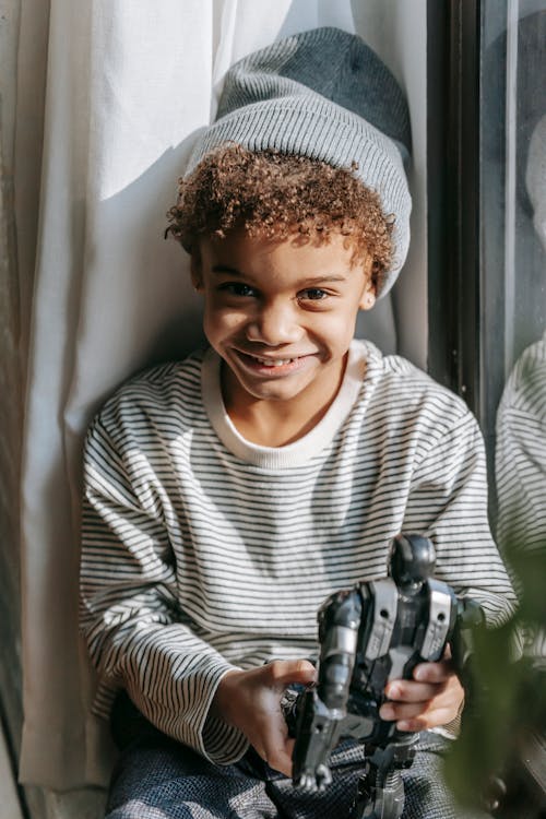 Smiling black boy with robot toy near window