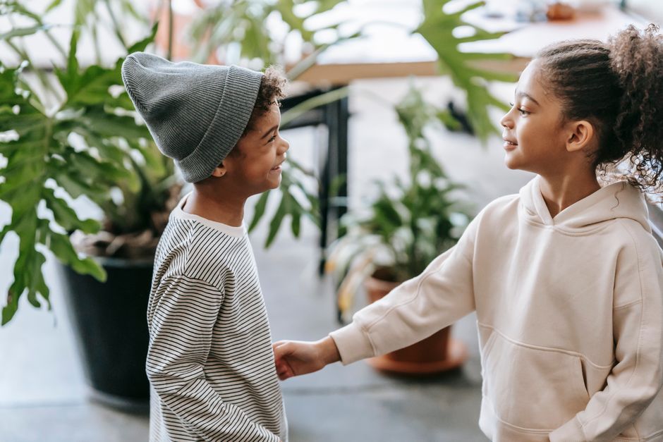 Seitenansicht eines positiven schwarzen Mädchens, das in einem hellen Zuhause den Bauch eines Jungen mit der Faust berührt, während es lässige Outfits in der Nähe von Topfpflanzen mit grünen Blättern trägt und dabei einander ansieht