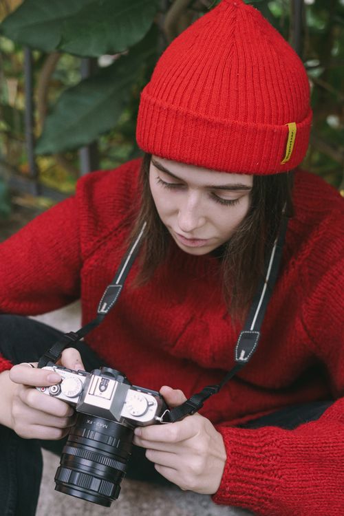 Free Focused female photographer in red outfit reviewing camera settings outdoors. Stock Photo