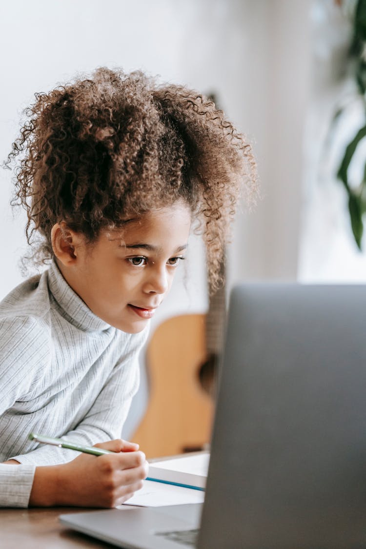 Cheerful Black Girl Writing On Paper While Browsing Laptop