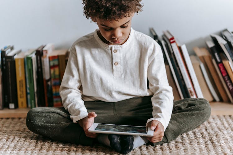 Crop Black Boy Browsing Tablet In Room