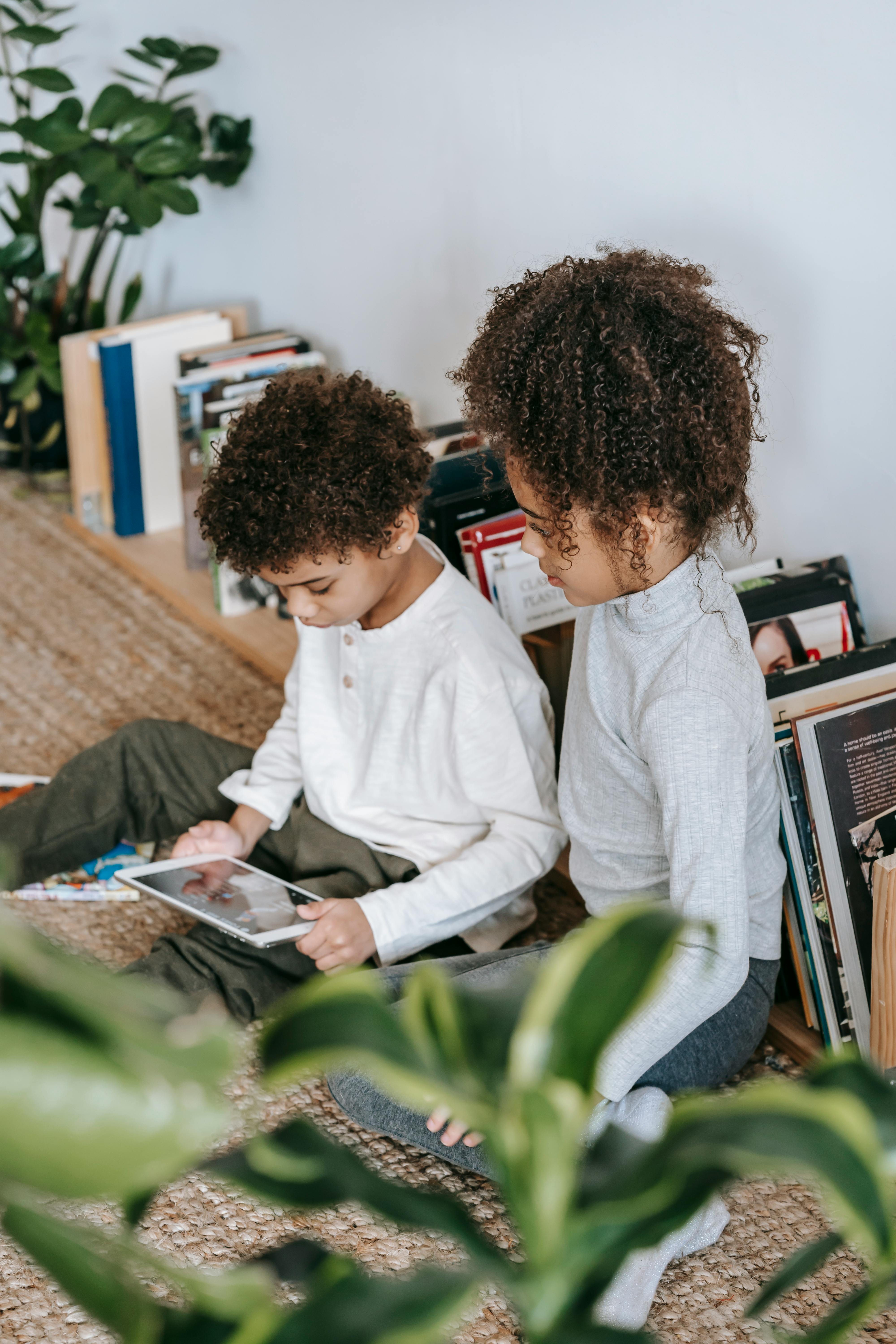 focused black children browsing tablet in room with books