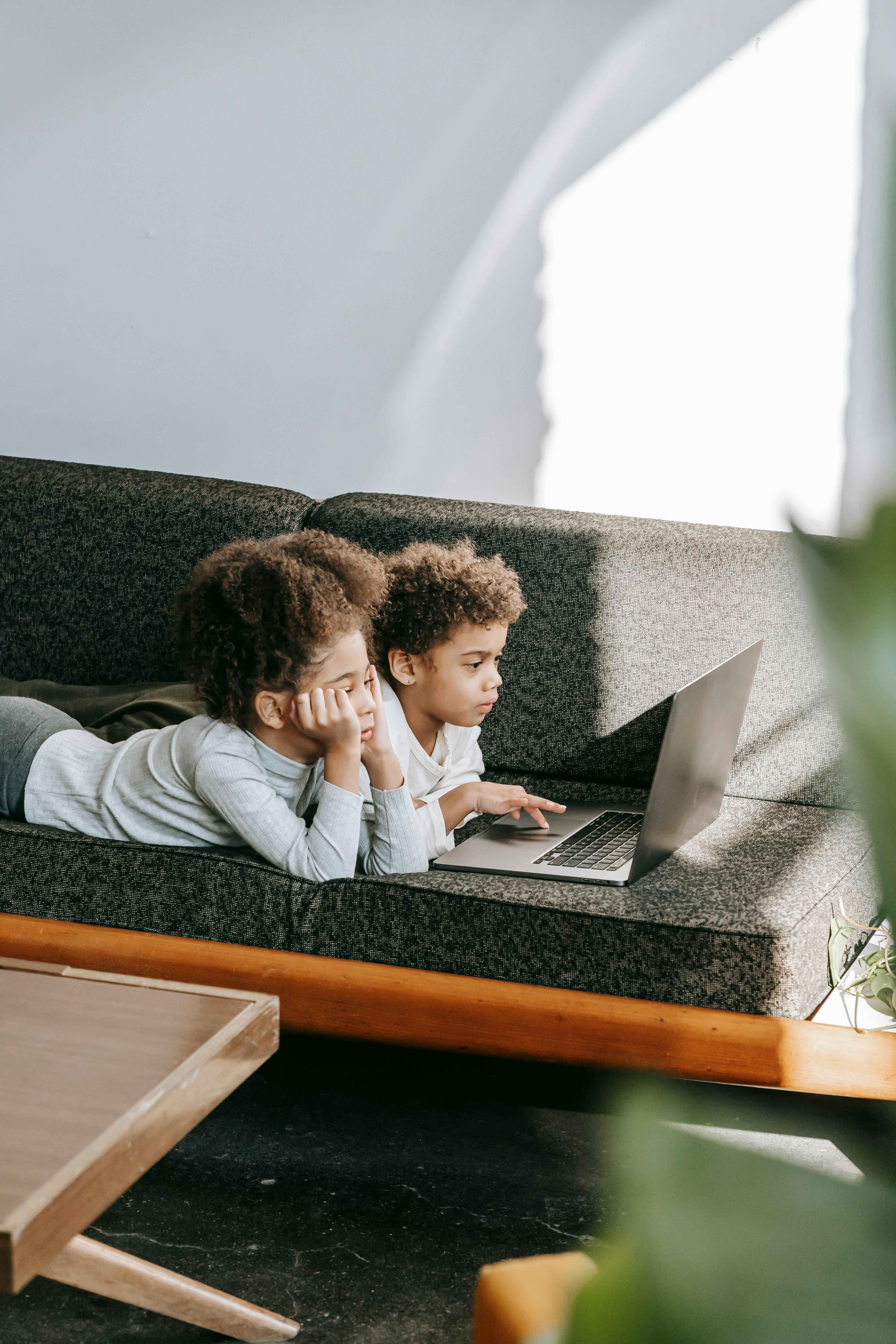 interested black children browsing laptop in living room
