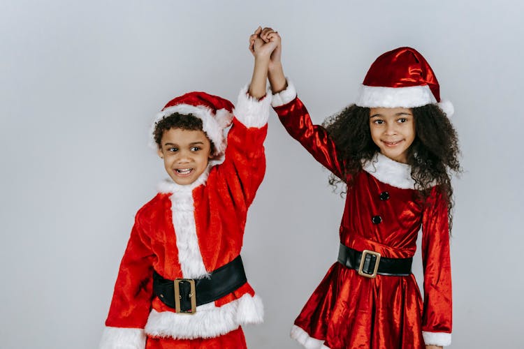 Smiling Black Siblings In Santa Costumes Holding Hands