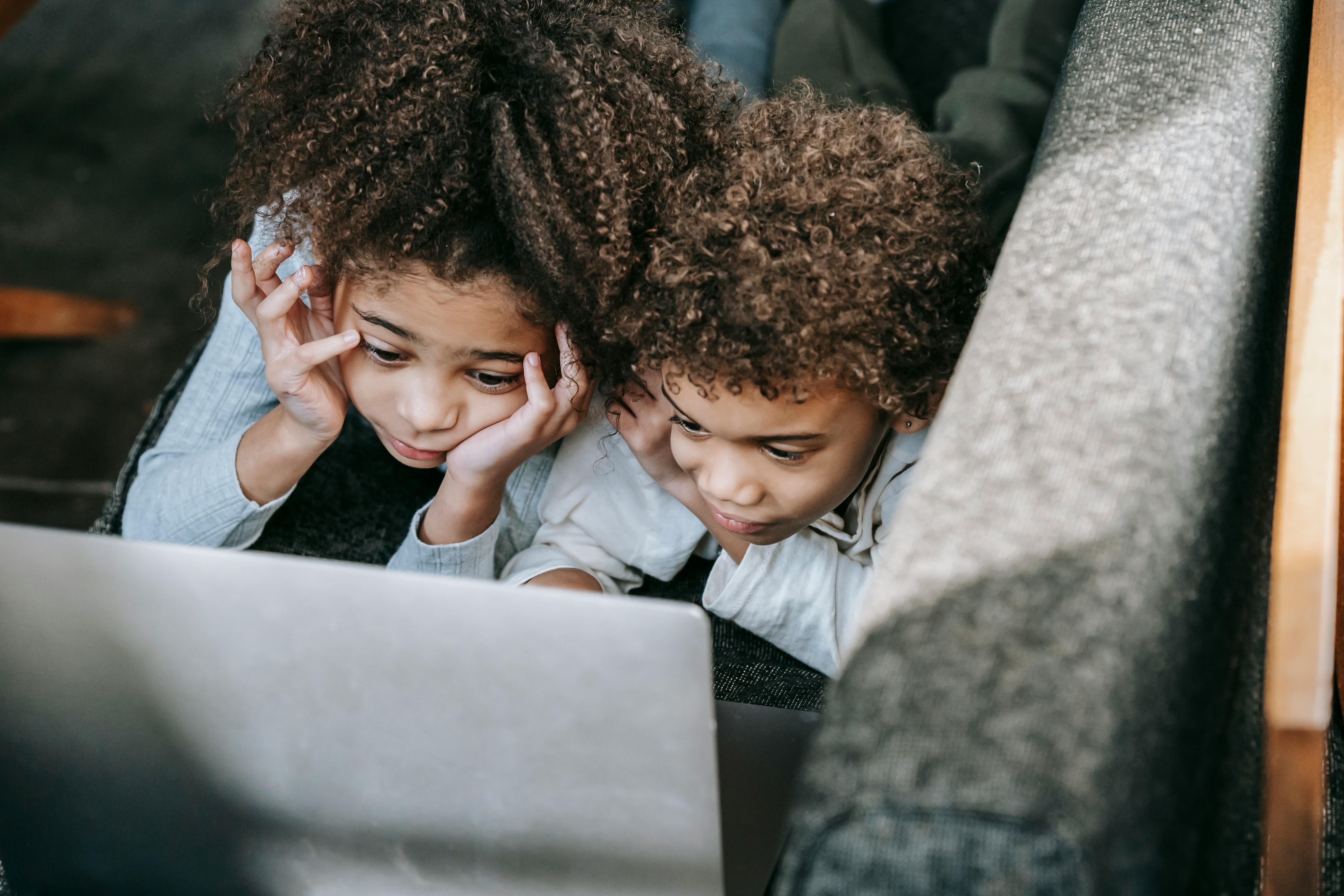 black siblings surfing internet on laptop on sofa at home