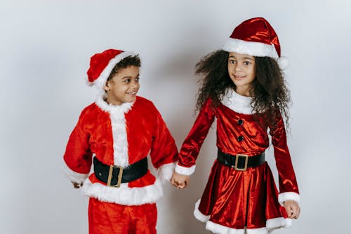 Smiling ethnic siblings in Santa costumes celebrating New Year holiday