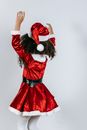 Back view of unrecognizable ethnic kid in Santa dress and hat having fun with raised arms during Christmas holiday