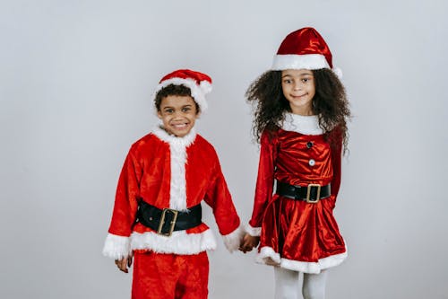 Free Sincere black sister with brother in bright Santa costumes celebrating New Year holiday on light background Stock Photo