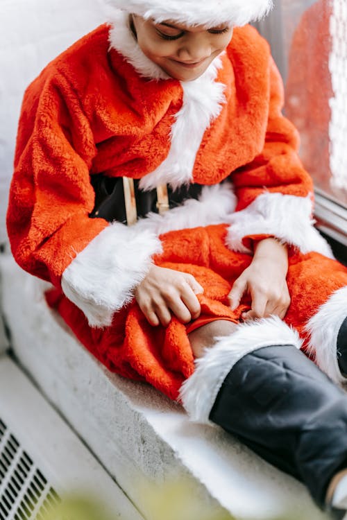 Crop smiling black boy in Santa costume on windowsill