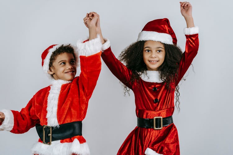 Excited Black Kids In Santa Costumes Jumping In Studio