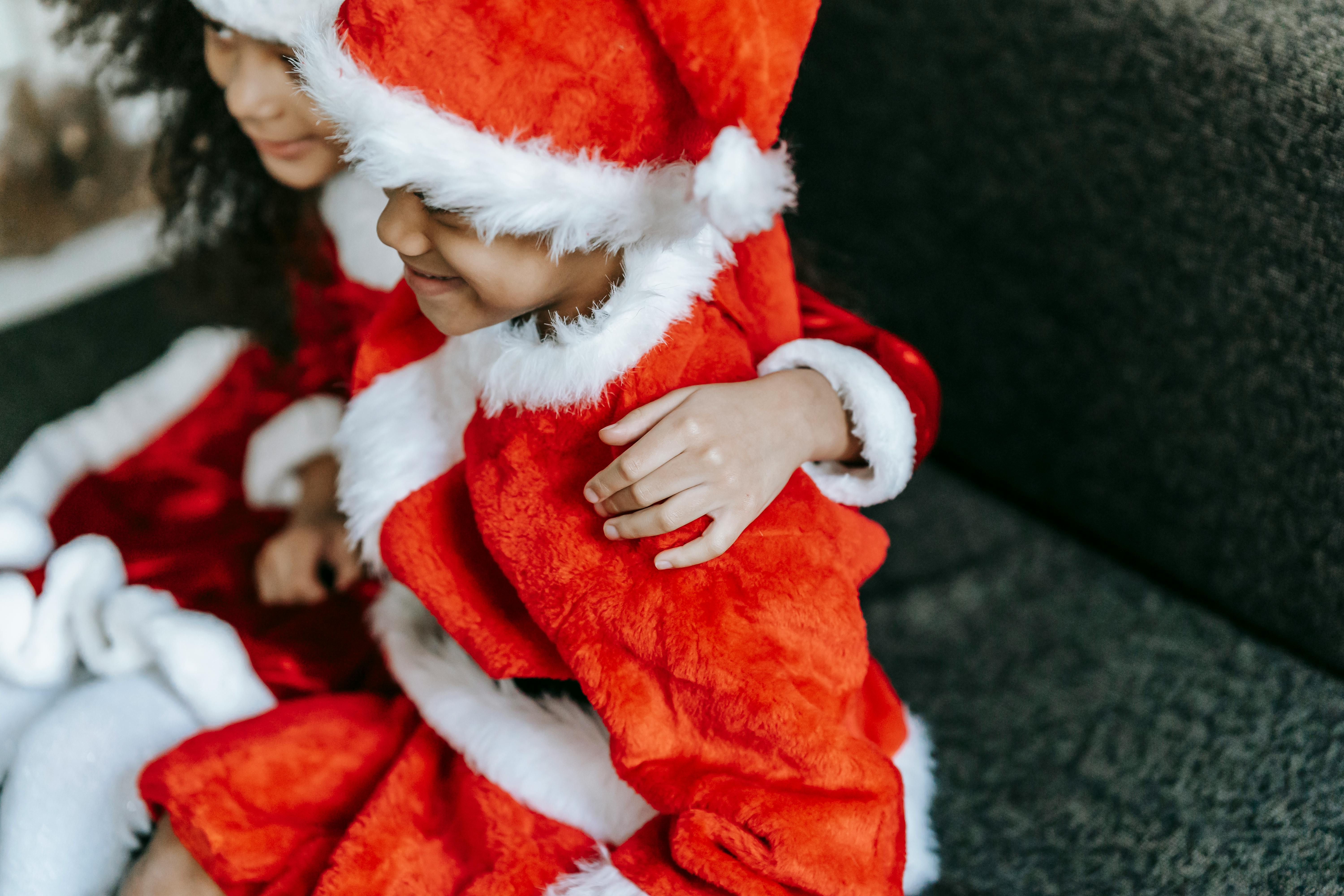 crop happy black siblings in santa costumes hugging on sofa