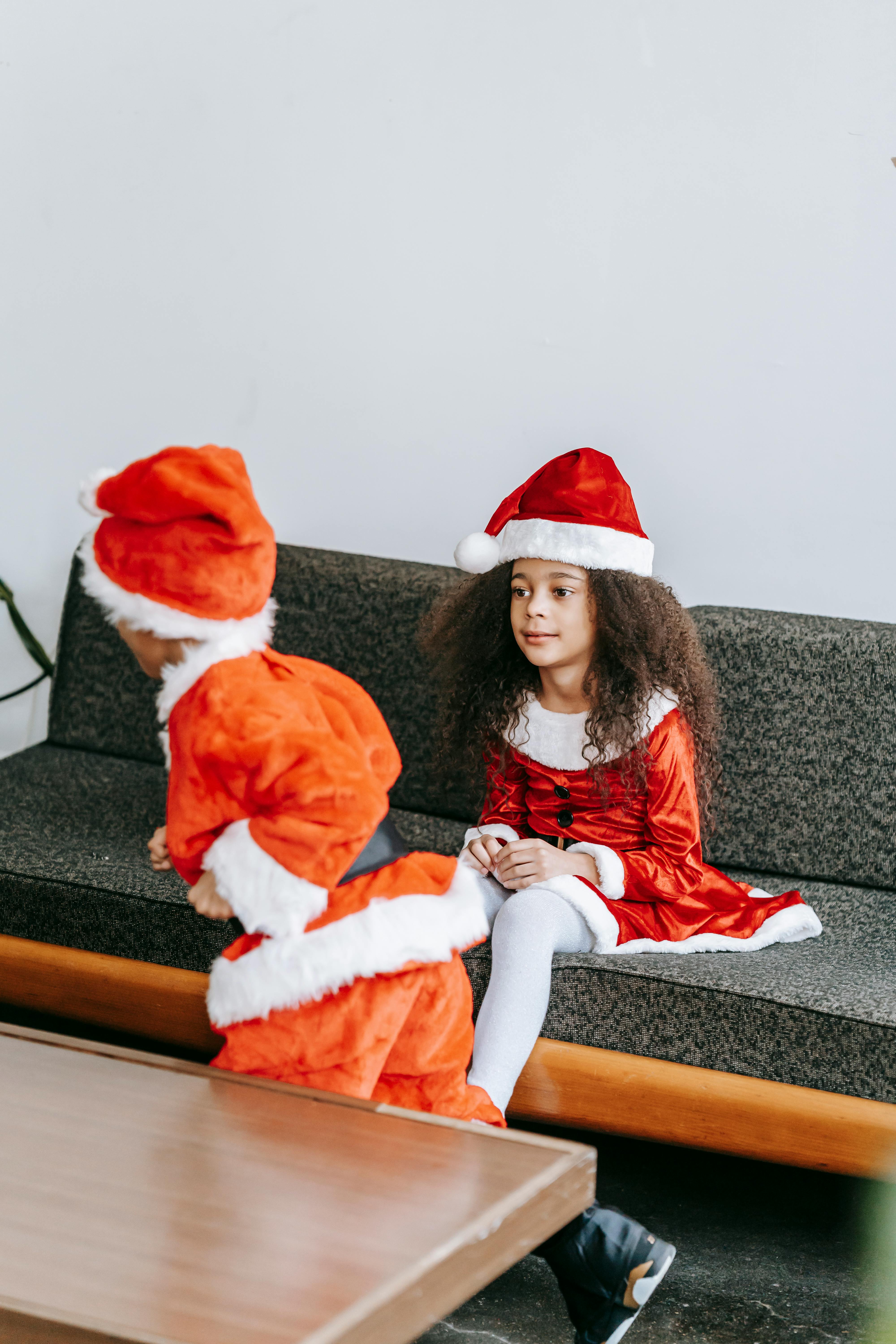 funny black siblings in santa clothes playing on sofa