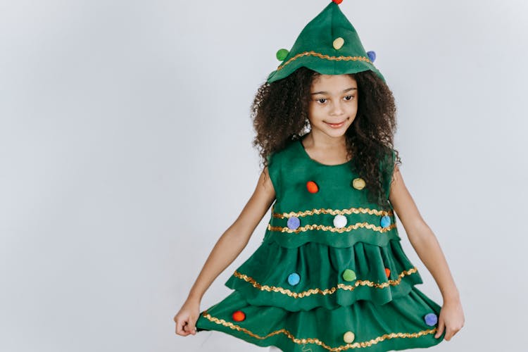 Smiling Girl In Christmas Tree Costume Standing In Light Studio