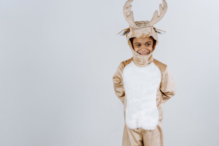 Cute Black Boy In Deer Costume Standing Against White Background