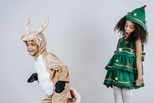 Cheerful African American siblings in Christmas tree and deer costumes playing and having fun together in light studio