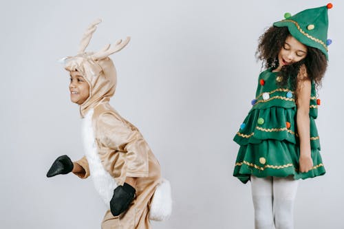 Adorable happy African American children wearing creative festive costumes playing and having fun together in light studio