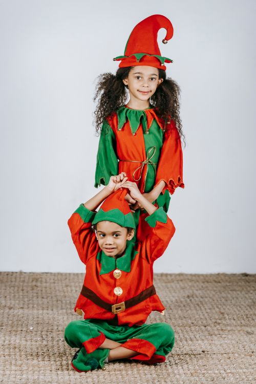 Free Full body of positive African American siblings in colorful elf outfits looking at camera in light room near white wall during Christmas holiday Stock Photo