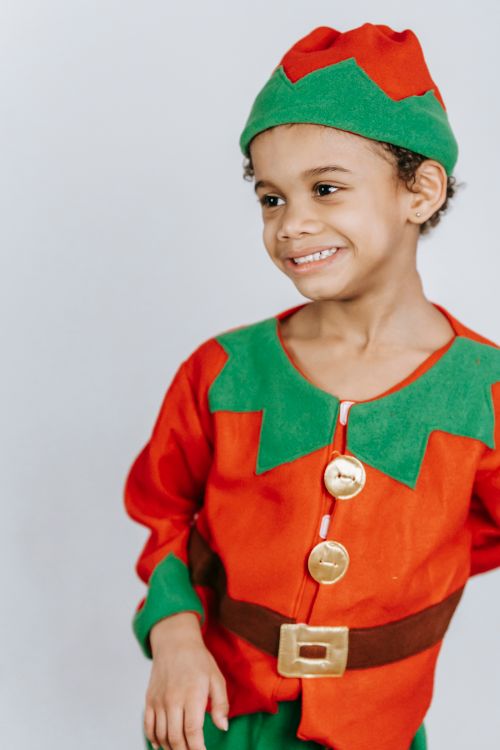 Free Cheerful African American boy wearing bright elf costume and headdress smiling and looking away while standing on white background during Christmas holiday Stock Photo