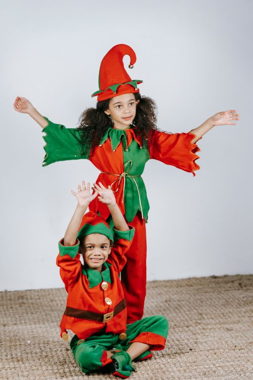 Free Full body of cute African American siblings with raised arms wearing colorful elf outfits in light room and looking away during Christmas holiday Stock Photo