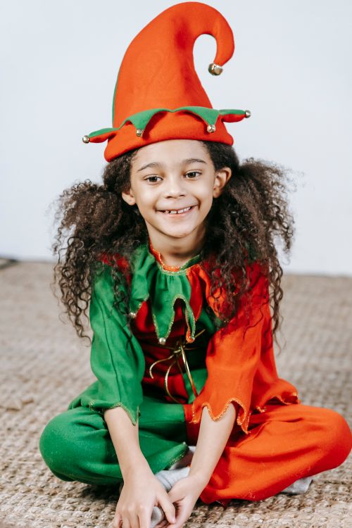 Free Adorable little positive African American girl in bright red and green costume of elf smiling Stock Photo