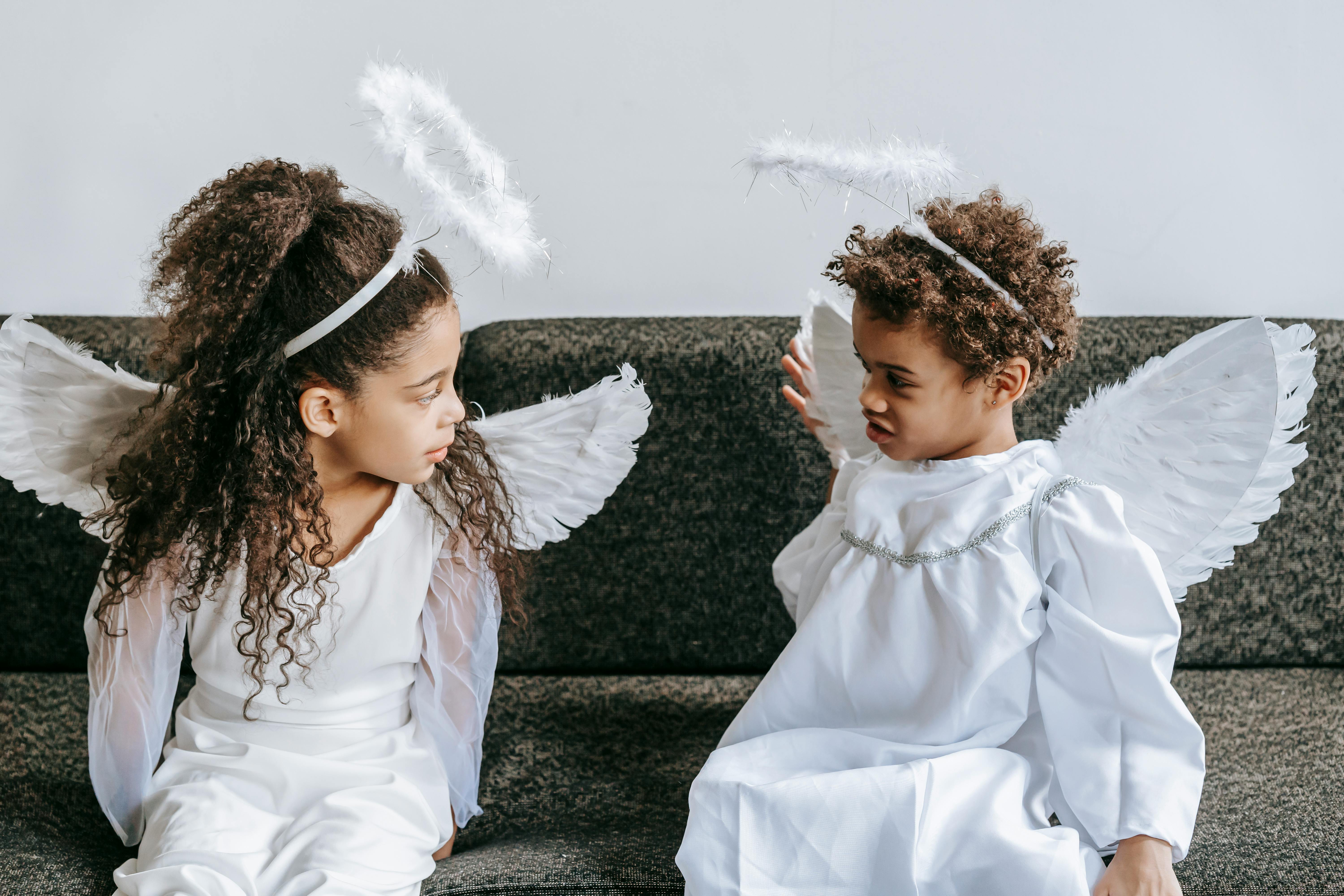 cute little black siblings in angels costumes playing on couch