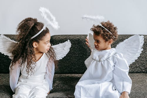 Free Cute little black siblings in angels costumes playing on couch Stock Photo