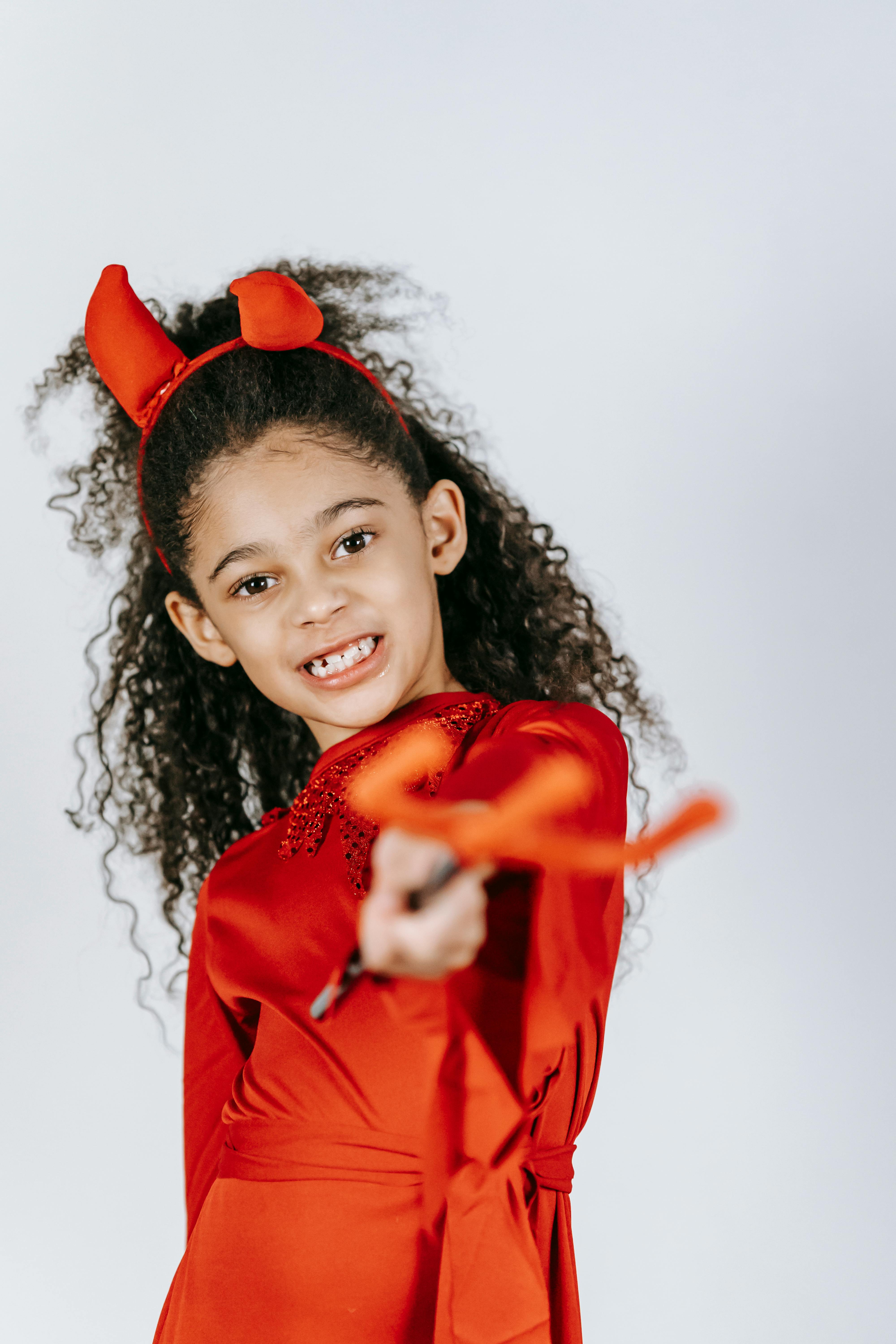 cute african american child in devil costume and horns showing pitchfork in white studio