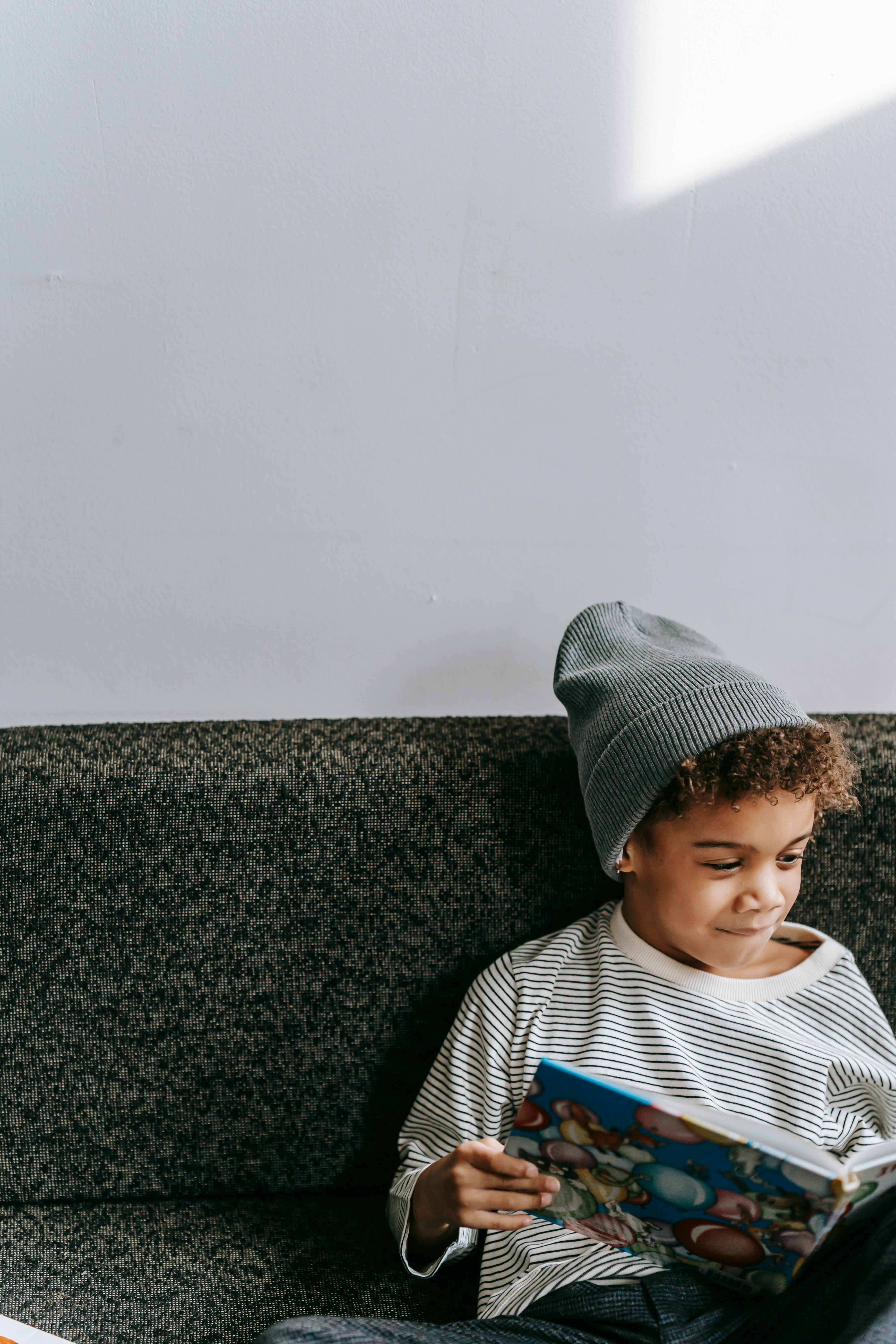 cute little black kid reading book on couch