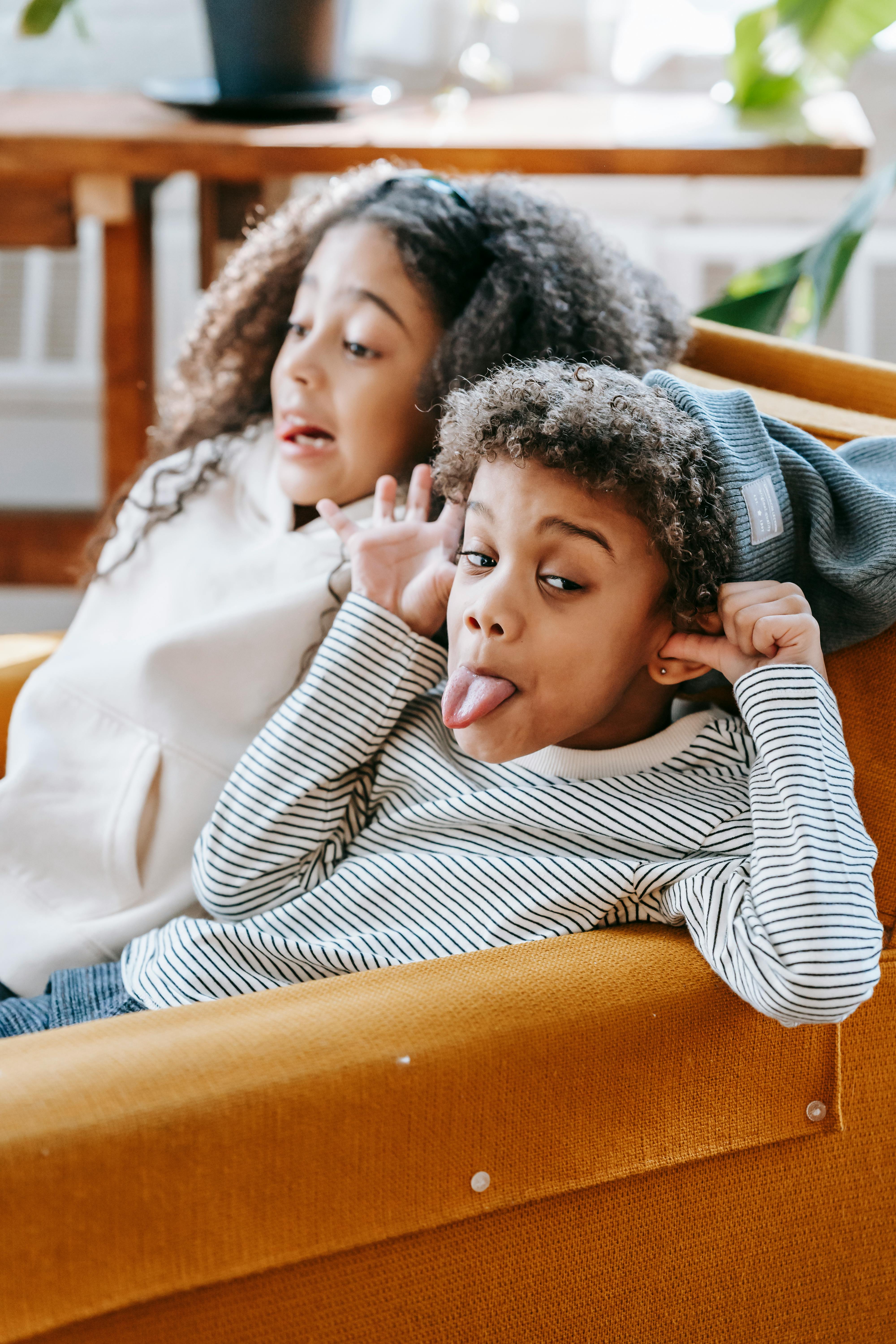 cute little black siblings making grimace on sofa