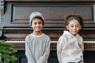 Adorable little African American boy and girl with curly hairs in casual outfits sitting near vintage wooden piano and looking at camera