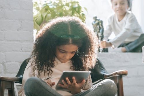 Serious ethnic little girl using tablet during weekend at home with sibling