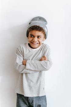 Adorable child with curly hair and beanie, smiling joyfully indoors against white background.