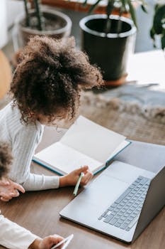 Young girl focusing on homework using a laptop, indicating remote learning.