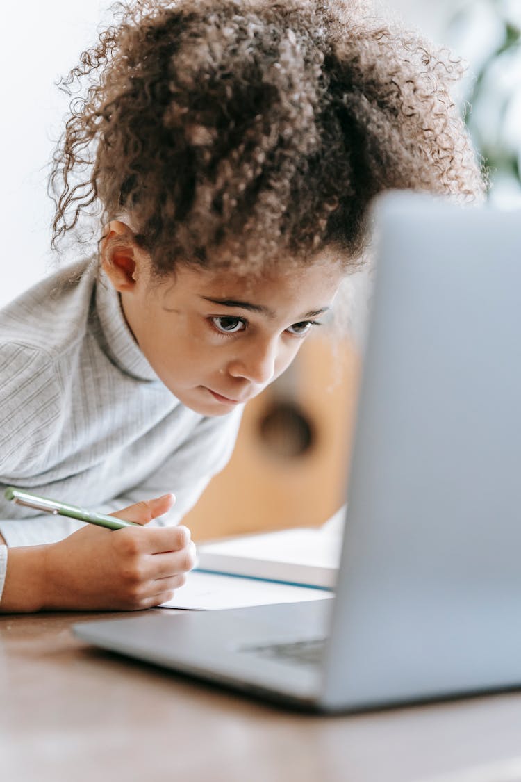 Concentrated Black Girl Using Laptop While Doing Homework