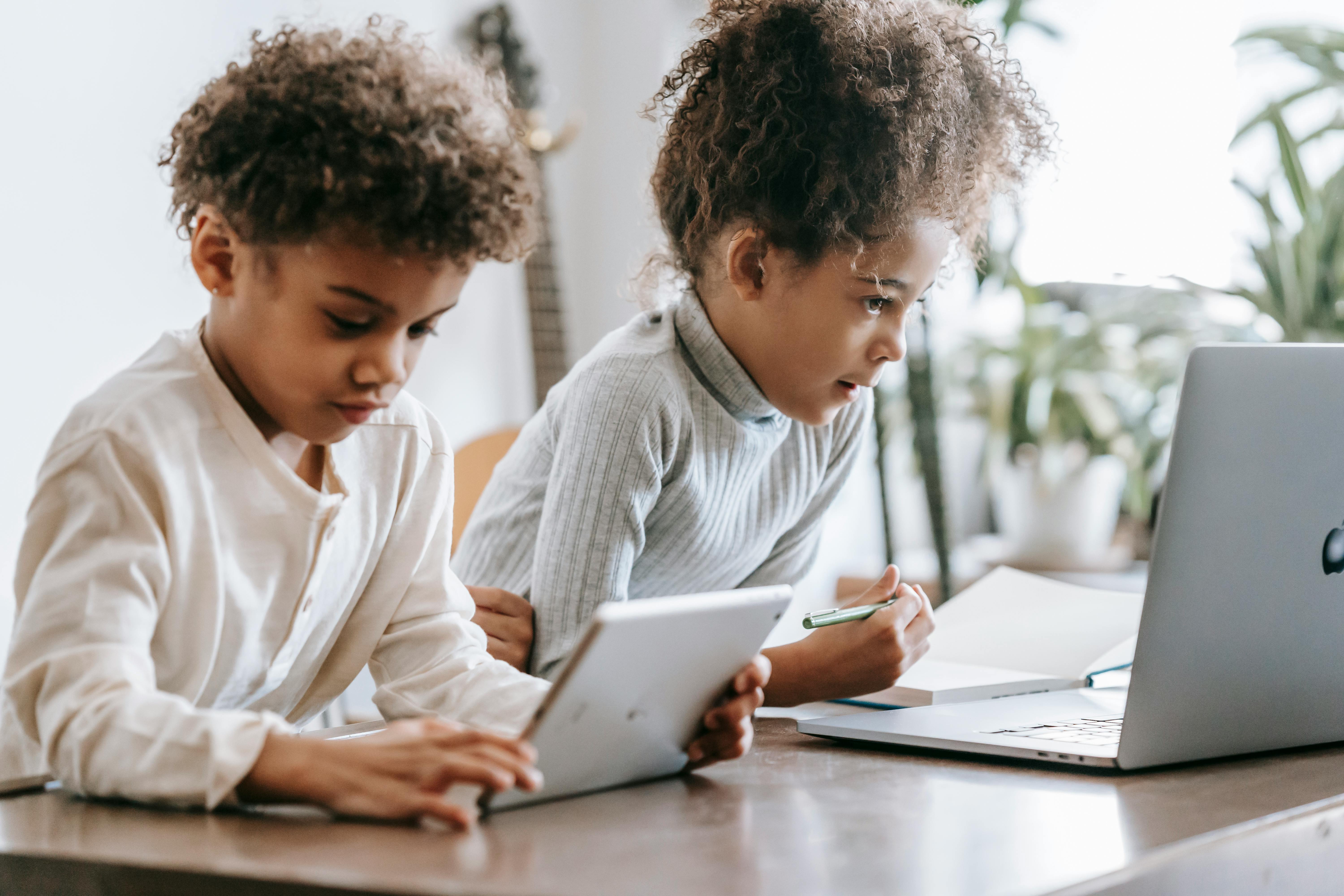 concentrated black children using laptop and tablet at home