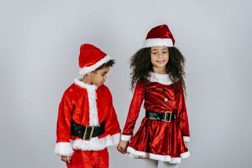 Cute African American boy and girl in bright red Santa costumes on white background