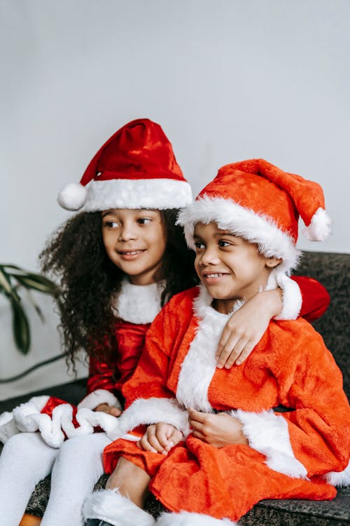 Happy little African American brother and sister smiling and looking away while celebrating Christmas