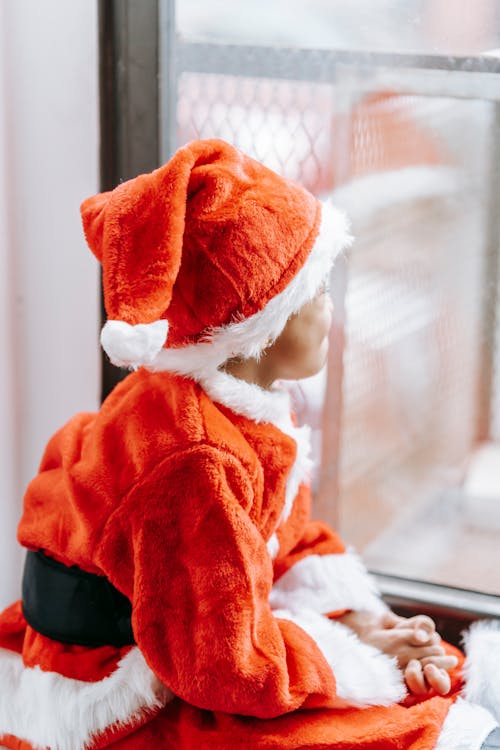 Side view of anonymous African American preschooler in red Santa costume looking away in window