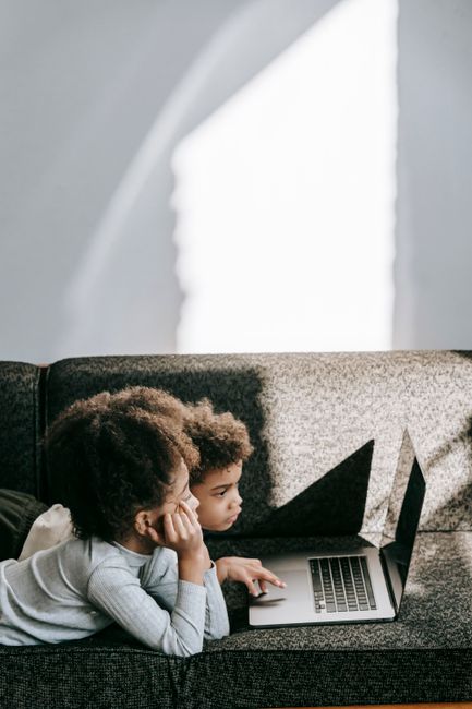 Side view of adorable little African American children browsing netbook with black screen in daytime