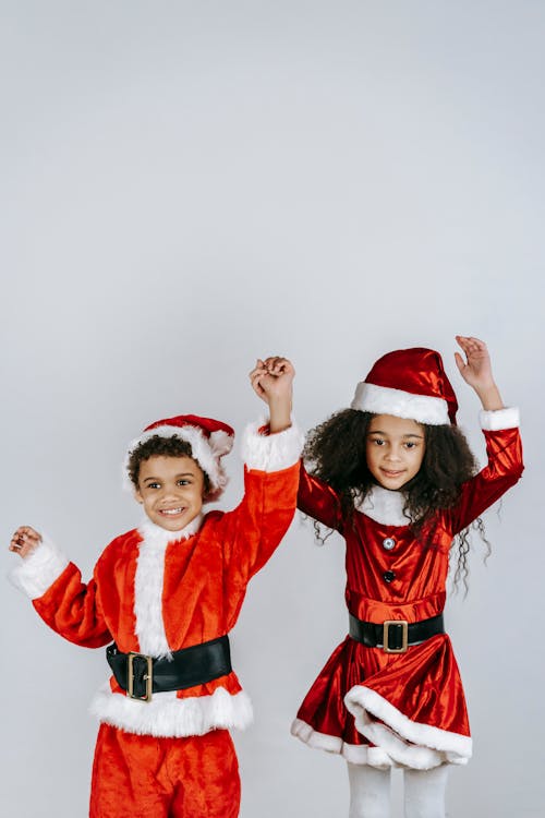 Positive black children in red Santa costumes dancing