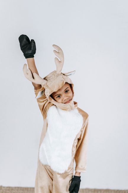 Cute cheerful African American boy with arm raised in soft funny reindeer costume on white background