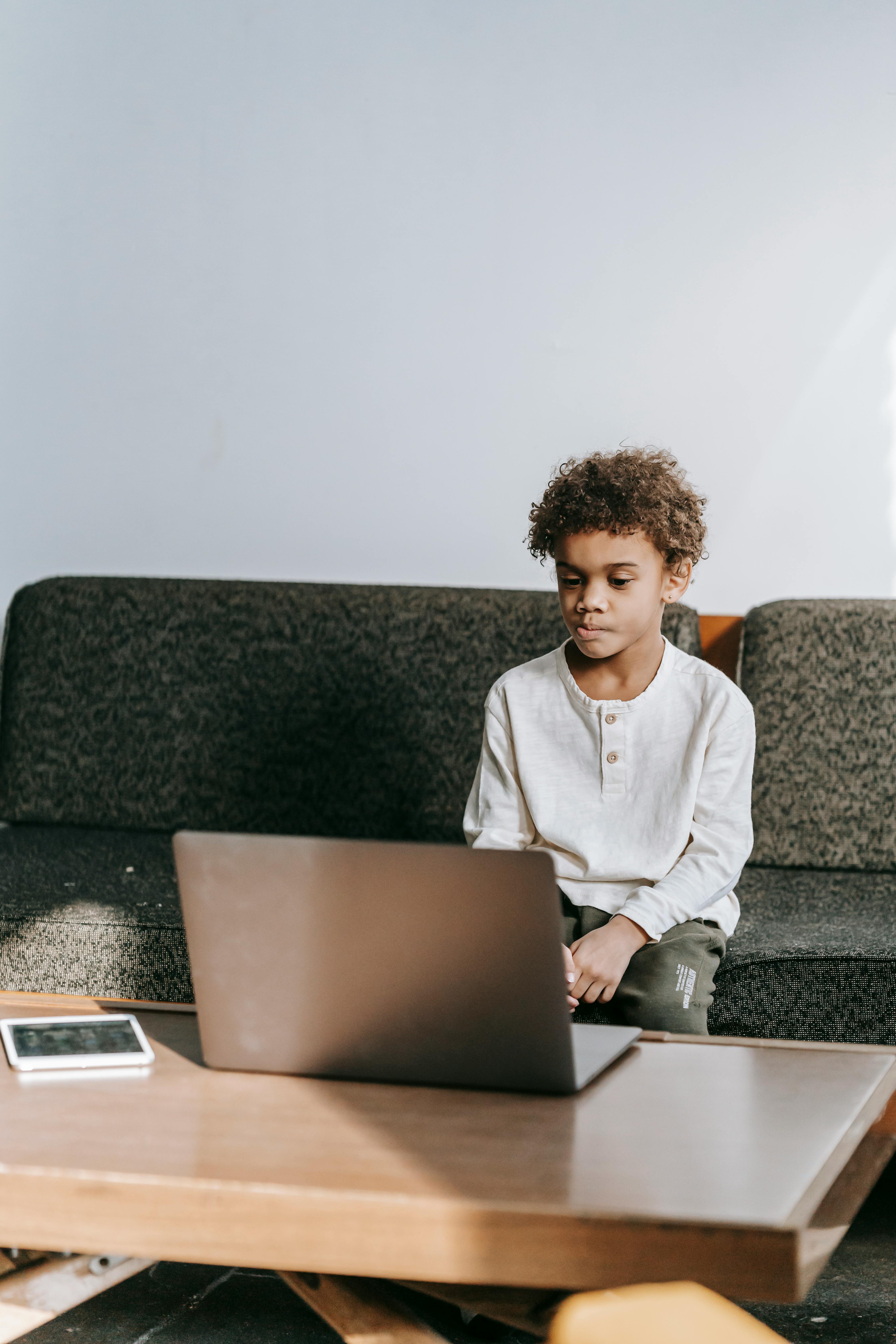 serious black boy using laptop at table on sofa